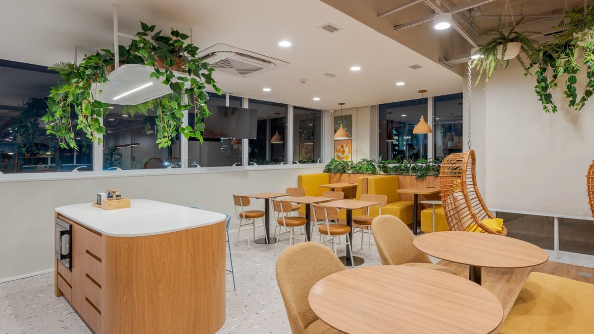 Área de convivência com mesas redondas, plantas suspensas e poltronas.